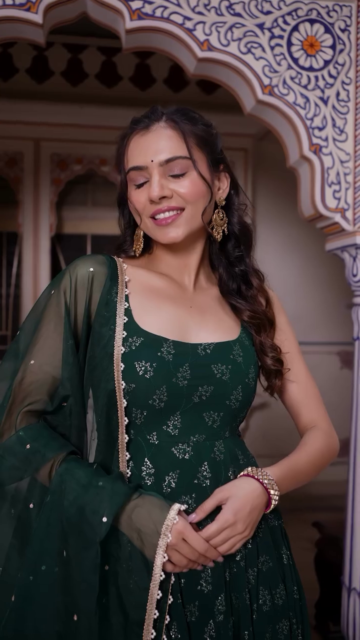 Elegantly Twirling in a Rich Green Anarkali Dress Adorned with Delicate Silver Embroidery, Paired with a Sheer Green Dupatta, Radiating Grace and Charm in a Traditional Setting