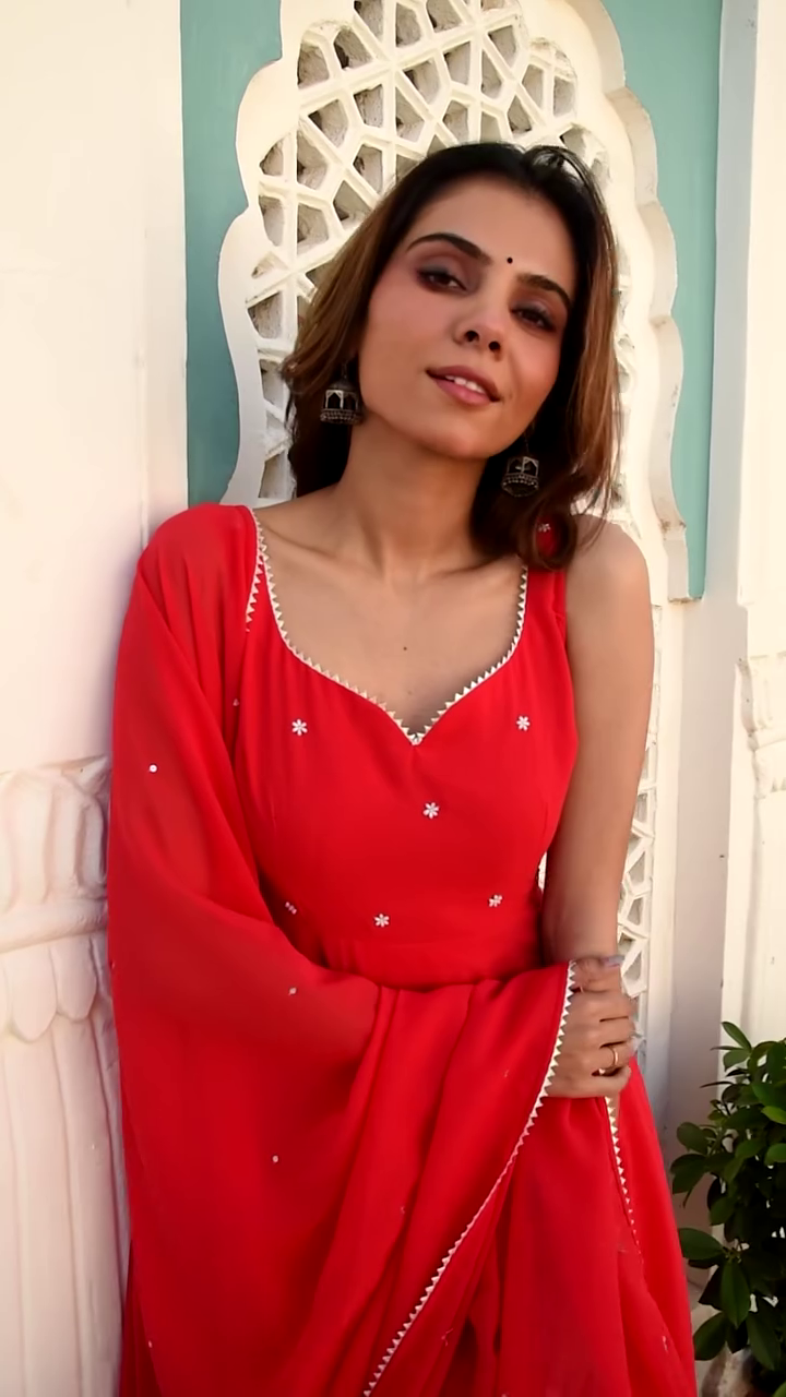 Radiating Elegance in a Bright Red Anarkali Dress, Adorned with Sparkling White Embellishments, Gracefully Twirling with a Matching Red Dupatta Against a Stunning Traditional Backdrop