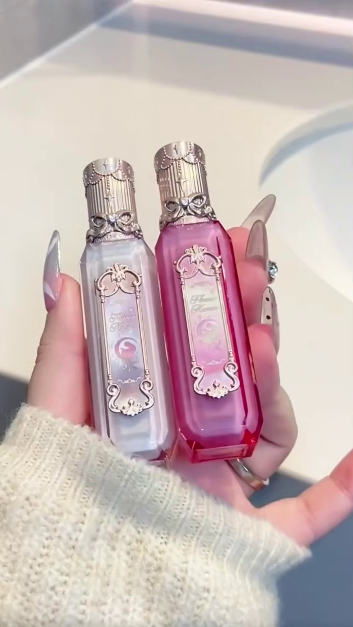 Two beautifully designed lipstick tubes in soft pastel colors, featuring intricate detailing on the cap, perfect for adding a touch of elegance and charm to your makeup collection.
