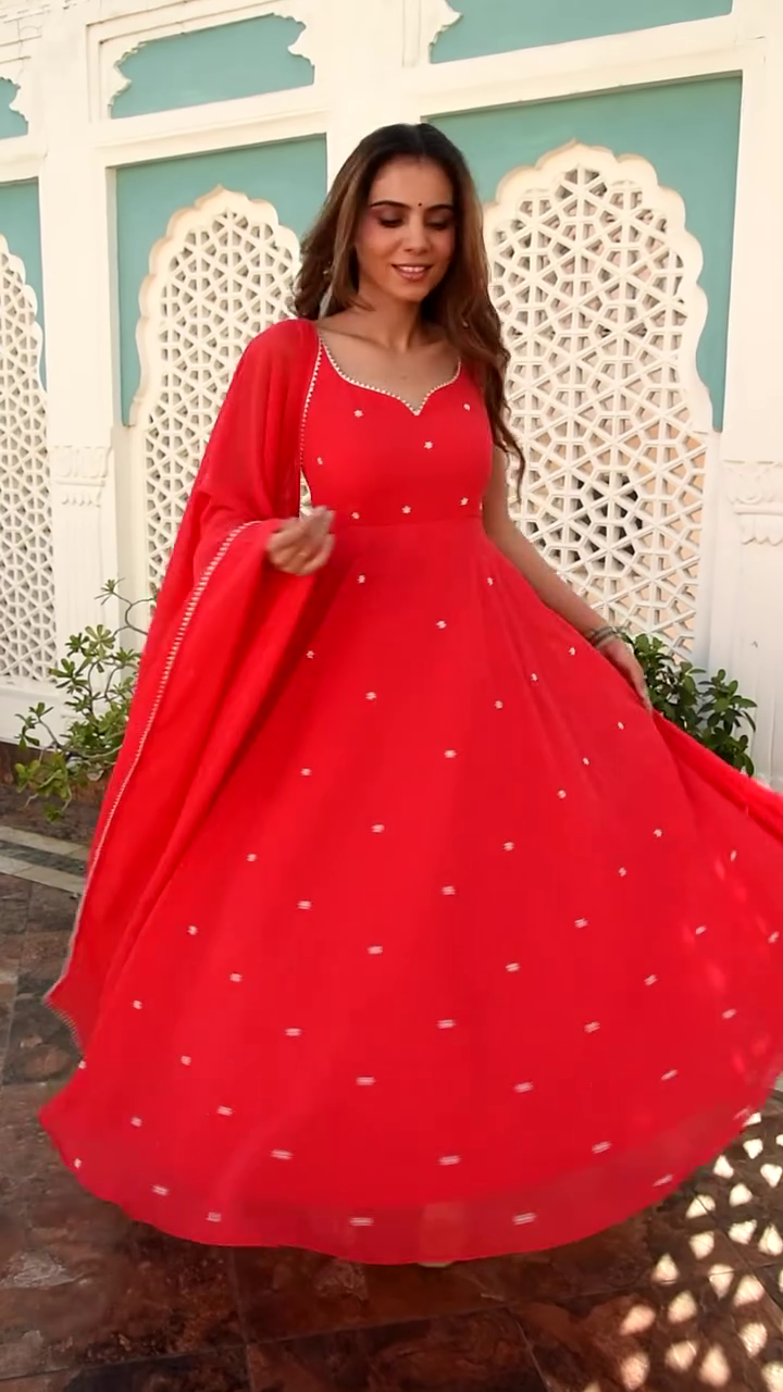 Radiating Elegance in a Bright Red Anarkali Dress, Adorned with Sparkling White Embellishments, Gracefully Twirling with a Matching Red Dupatta Against a Stunning Traditional Backdrop