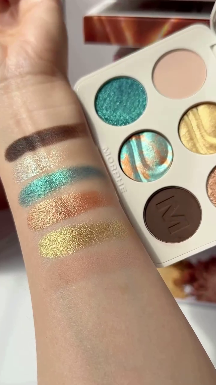 Swatches of Vibrant Eyeshadow Shades from the Morphe Palette, Featuring Sparkling Teals, Shimmery Oranges, Golds, and a Rich Brown, Perfect for Creating Stunning Eye Looks